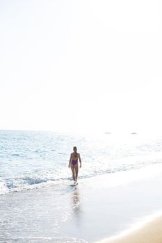 Beautiful woman with a toned body in a bright swimsuit walks along the sandy beach. Summer vacation at the sea. Mediterranean Turkish Sea. Selective focus
