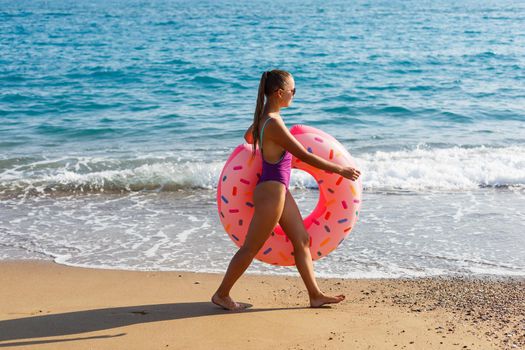 Woman on the beach walks with an inflatable ring in the sea, walks relaxing in a tropical paradise for relaxation. Young model sunbathing on summer vacation.