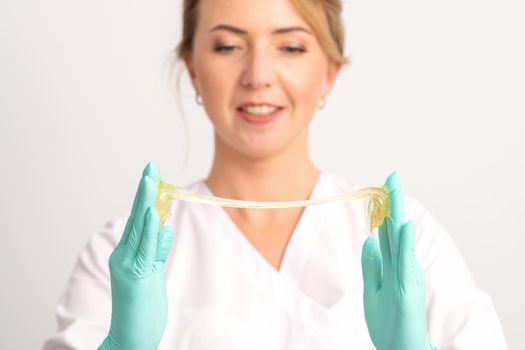 Young caucasian smiling female beautician holding wax for depilation over white background. Yellow sugar paste in hands master of depilation. Epilation concept