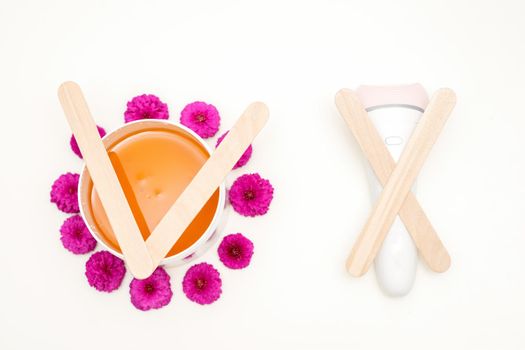 Waxing, depilation concept. Flat lay of the white cosmetic jar with sugar paste and epilator with wooden sticks lying on white background