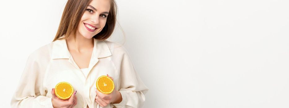 Young Caucasian smiling woman holding slices orange over isolated white background, breast health concept