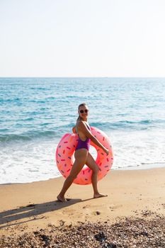 Woman on the beach walks with an inflatable ring in the sea, walks relaxing in a tropical paradise for relaxation. Young model sunbathing on summer vacation.