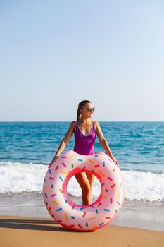 Attractive young woman in a bright swimsuit posing on the beach with an inflatable ring. Beautiful blond woman with long hair relaxing by the ocean. The concept of a sports model, swimwear