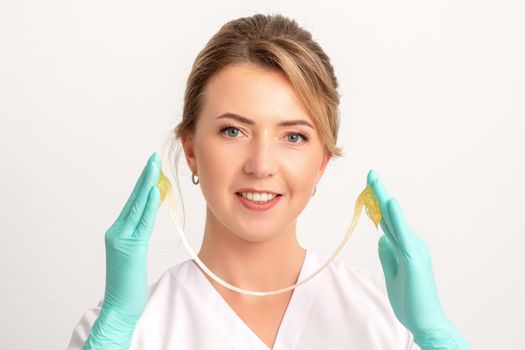 Young caucasian smiling female beautician holding wax for depilation over white background. Yellow sugar paste in hands master of depilation. Epilation concept