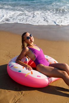 Attractive young woman in a bright swimsuit posing on the beach with an inflatable ring. Beautiful blond woman with long hair relaxing by the ocean. The concept of a sports model, swimwear