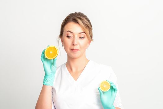 Smiling female nutritionist holding a sliced orange, looking at camera over white background, healthy diet concept