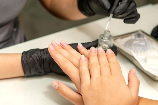 Manicure painting process. Manicure master paint the nails with transparent varnish in a nail salon, close up