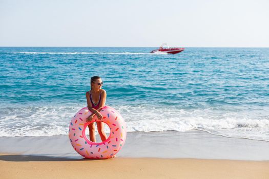 Attractive young woman in a bright swimsuit posing on the beach with an inflatable ring. Beautiful blond woman with long hair relaxing by the ocean. The concept of a sports model, swimwear