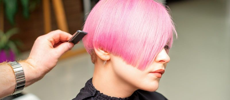 A hairdresser is combing the dyed pink short hair of the female client in a hairdresser salon