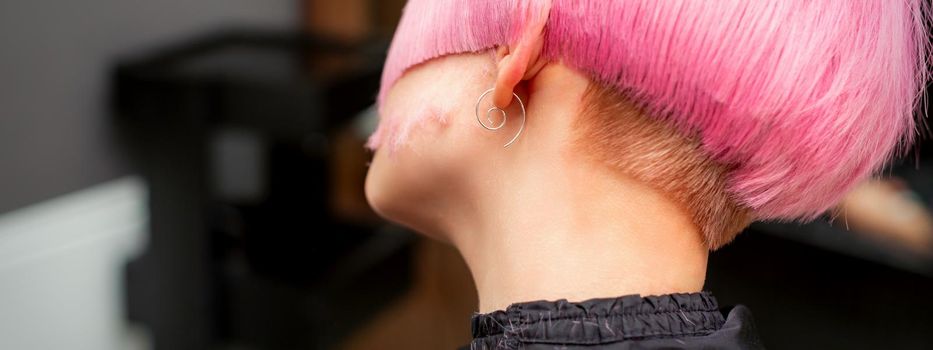 Styling and cutting dyed pink hair of young model back view in a hairdressing salon. Pink short hairstyle