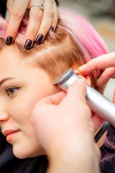 Hairdresser shaves female temple with pink hair by electric shaver in a hairdresser salon, close up