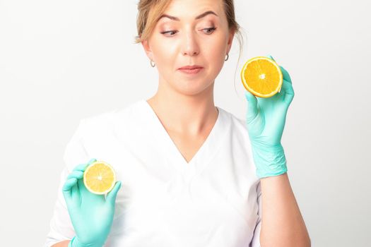 Smiling female nutritionist holding a sliced orange, looking at camera over white background, healthy diet concept