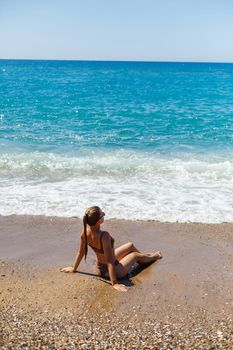 Summer lifestyle. Beautiful woman with a slim tanned body in a bikini swimsuit enjoying life and lying on the sand on the beach of a tropical island. Selective focus