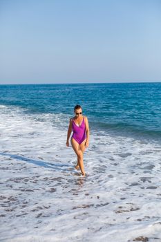 A young beautiful woman with a toned body in a bright swimsuit walks along the sandy beach. Summer vacation at the sea. Mediterranean Turkish Sea. Selective focus