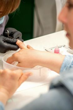 Manicure master removes cuticles from female nails with scissors wearing protective gloves in manicure salon