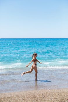A slender beautiful young woman in a swimsuit walks along the beach by the sea. Summer vacation concept. Selective focus