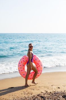 Woman on the beach walks with an inflatable ring in the sea, walks relaxing in a tropical paradise for relaxation. Young model sunbathing on summer vacation.