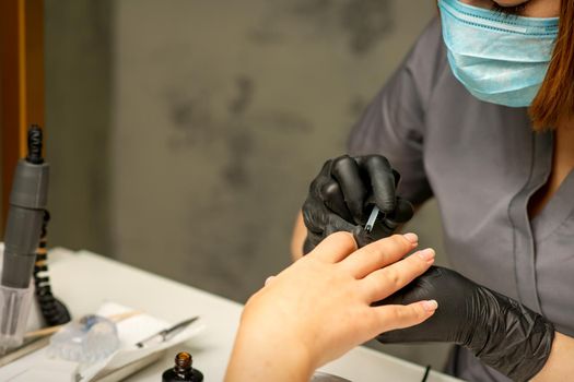 Manicure painting process. Manicure master paint the nails with transparent varnish in a nail salon, close up