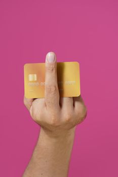 Aggressive hand gesture fuck you male hand holding debit, credit card between fingers isolated on pink background. Banking, finances concept. Male hand with bank card.