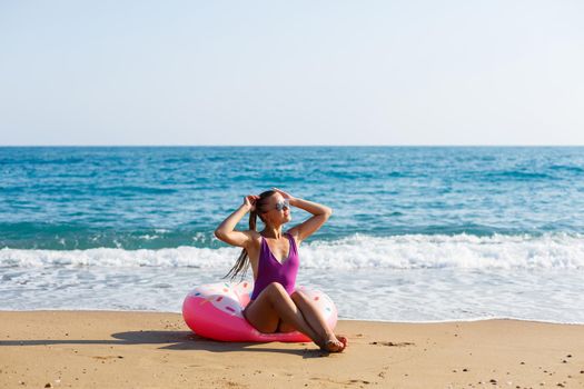 Attractive young woman in a bright swimsuit posing on the beach with an inflatable ring. Beautiful blond woman with long hair relaxing by the ocean. The concept of a sports model, swimwear