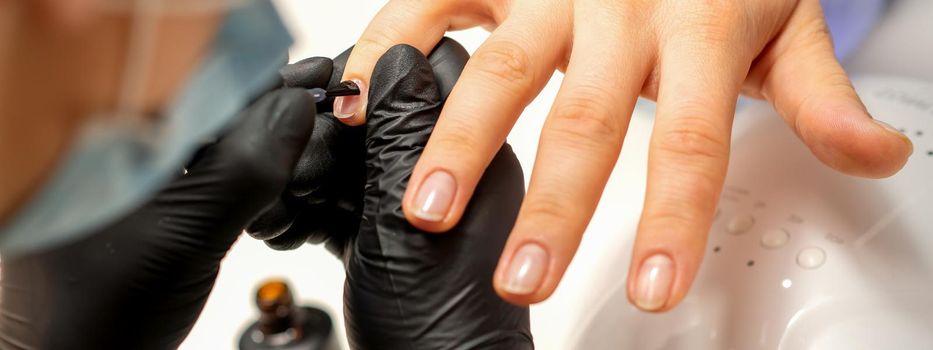 Manicure painting process. Manicure master paint the nails with transparent varnish in a nail salon, close up