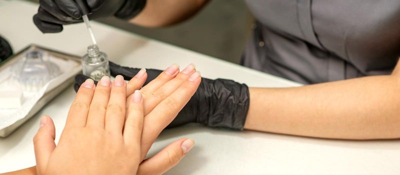 Manicure painting process. Manicure master paint the nails with transparent varnish in a nail salon, close up