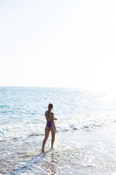 A young beautiful woman with a toned body in a bright swimsuit walks along the sandy beach. Summer vacation at the sea. Mediterranean Turkish Sea. Selective focus