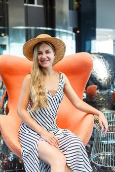 A beautiful young woman in a dress and a hat is sitting in the lobby of a luxury hotel. She is on vacation.