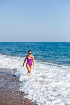 A young beautiful woman with a toned body in a bright swimsuit walks along the sandy beach. Summer vacation at the sea. Mediterranean Turkish Sea. Selective focus