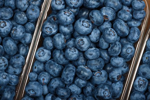 Close up fresh blueberry berries in plastic containers in brown cardboard box on retail display, elevated top view, directly above