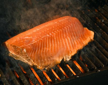 Close up searing and smoking salmon fish fillet on open fire outdoor grill with cast iron metal grate, high angle view