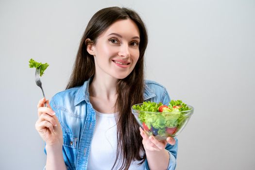 Happy beautiful young woman eats salad with lettuce, tomato and olives.