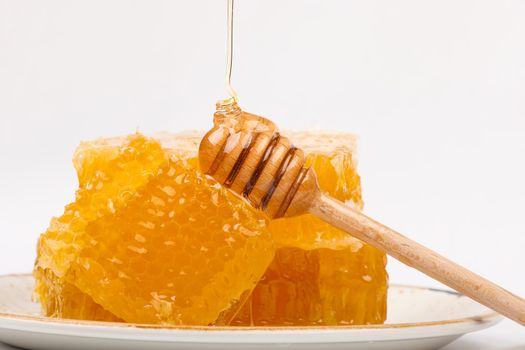 Close up stack of several fresh cut golden comb honey slices and natural wooden dipper on plate isolated on white background, low angle, side view