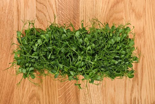 Close up fresh green pea microgreen sprouts on brown wooden cutting board background, elevated top view, directly above