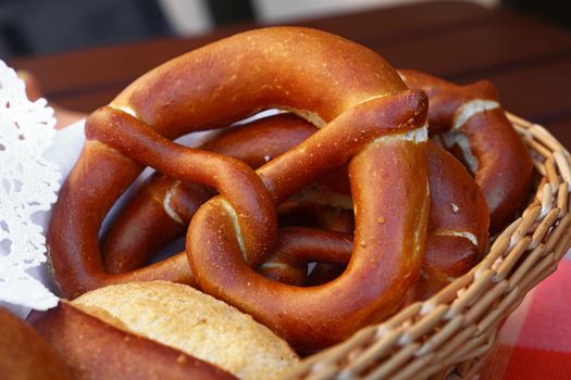 Close up several traditional German pretzel bread knots and fresh buns in bread basket on table, high angle view