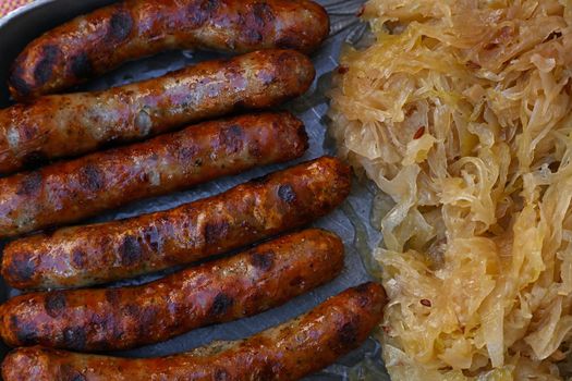 Close up portion of grilled Nuremberg Bratwurst sausages with side dish of sauerkraut on metal pewter plate, elevated top view, directly above