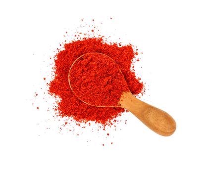 Close up one wooden scoop spoon full of red chili pepper, paprika or sundried tomato powder spilled and spread around isolated on white background, elevated top view, directly above