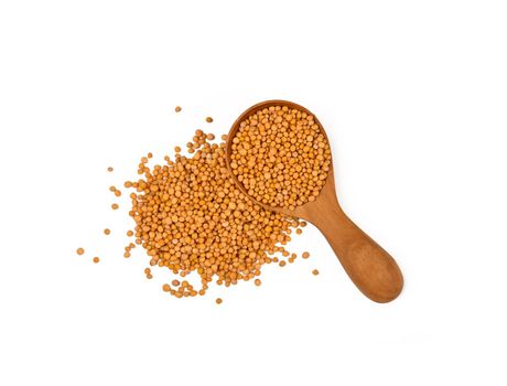 Close up one wooden scoop spoon full of wholegrain yellow mustard seeds, heap spilled around, isolated on white background, elevated top view, directly above