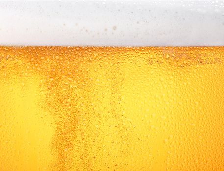 Close up background texture of pouring lager beer with bubbles and froth in frosty glass with drops, low angle side view
