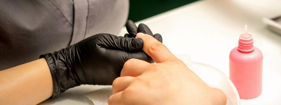 Close up professional manicure master holds the female hand of the customer and disinfects nails in a nail salon