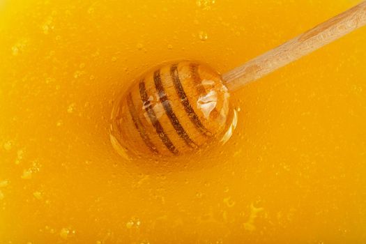 Close up one wooden honey dipper spoon in bowl of fresh thick fluid acacia honey, high angle view