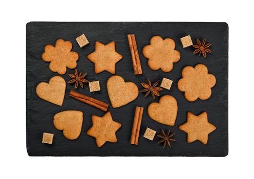 Close up heart and star shaped Christmas gingerbread cookies with cinnamon and star anise spices on black slate isolated on white background, elevated top view, directly above