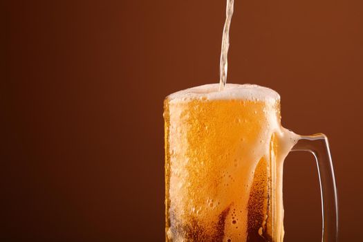 Close up pouring lager beer with white froth and bubbles in glass mug over dark brown background with copy space, low angle side view