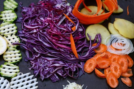 Close up assorted cut and sliced fresh vegetables on black cooking board, high angle view