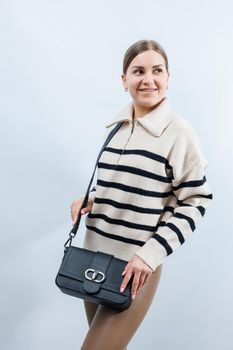 Beautiful young woman posing on a white background with a black handbag over her shoulder. A woman is holding a black leather shoulder bag. Women's fashion concept.