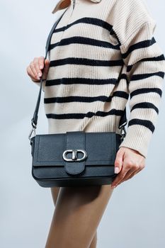 Beautiful young woman posing on a white background with a black handbag over her shoulder. A woman is holding a black leather shoulder bag. Women's fashion concept.