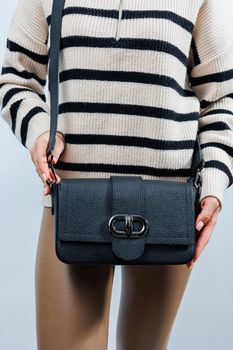 Beautiful young woman posing on a white background with a black handbag over her shoulder. A woman is holding a black leather shoulder bag. Women's fashion concept.