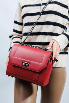 Small red leather bag in a female hand on a white background. Shoulder bag. Woman with a red handbag. Style, fashion, vintage and elegance.