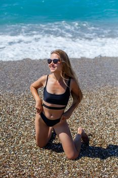 Amazing woman in a swimsuit with a beautiful athletic body walks and poses on the white sandy beach. A tanned young woman with long hair is resting and sunbathing. Charming model posing near the sea
