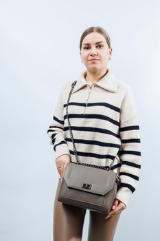 Small beige leather bag in a female hand on a white background. Shoulder bag. Woman with a beige handbag. Style, fashion, vintage and elegance.